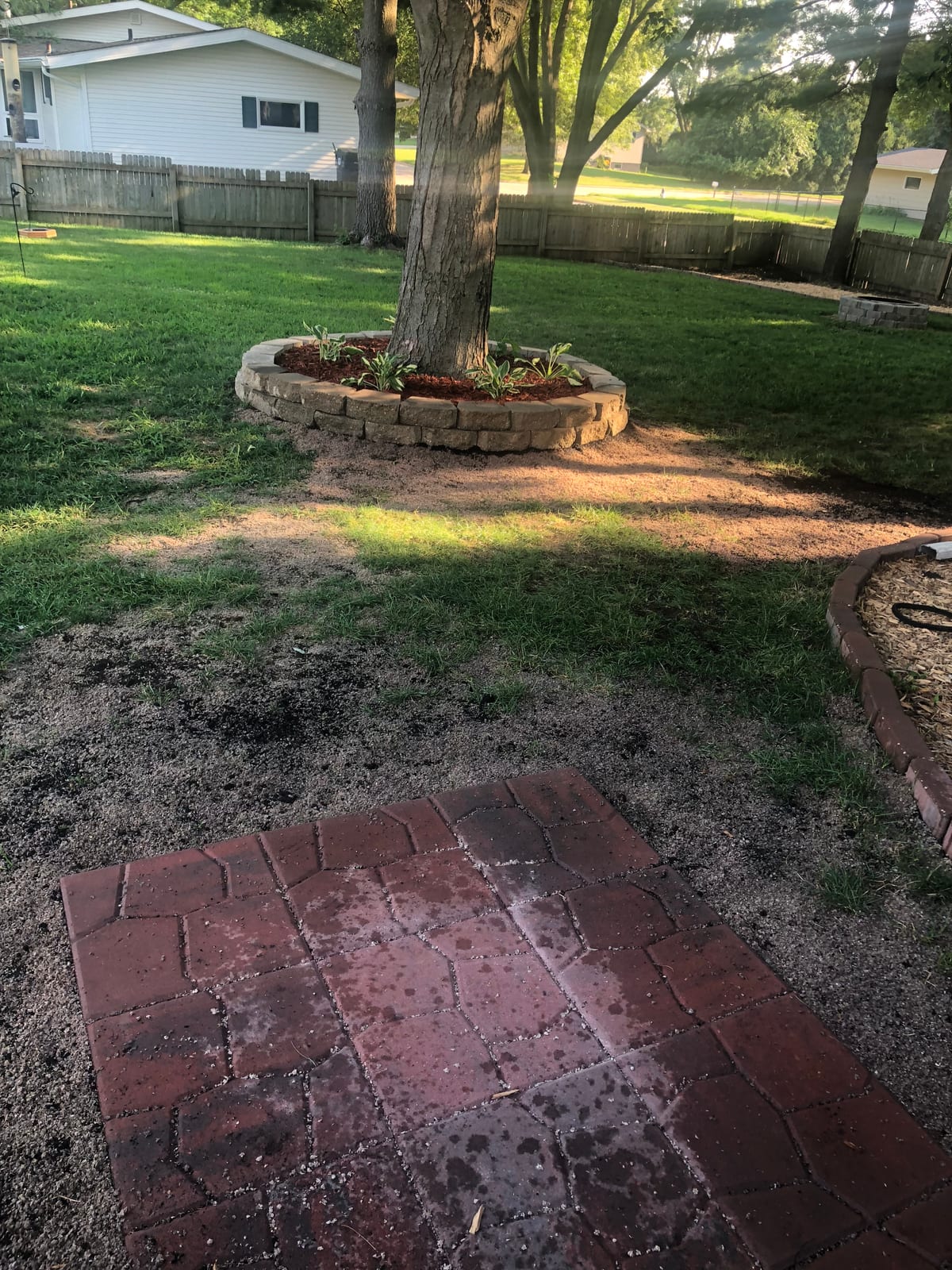 Stone planter and brick paver patio set into the side lawn