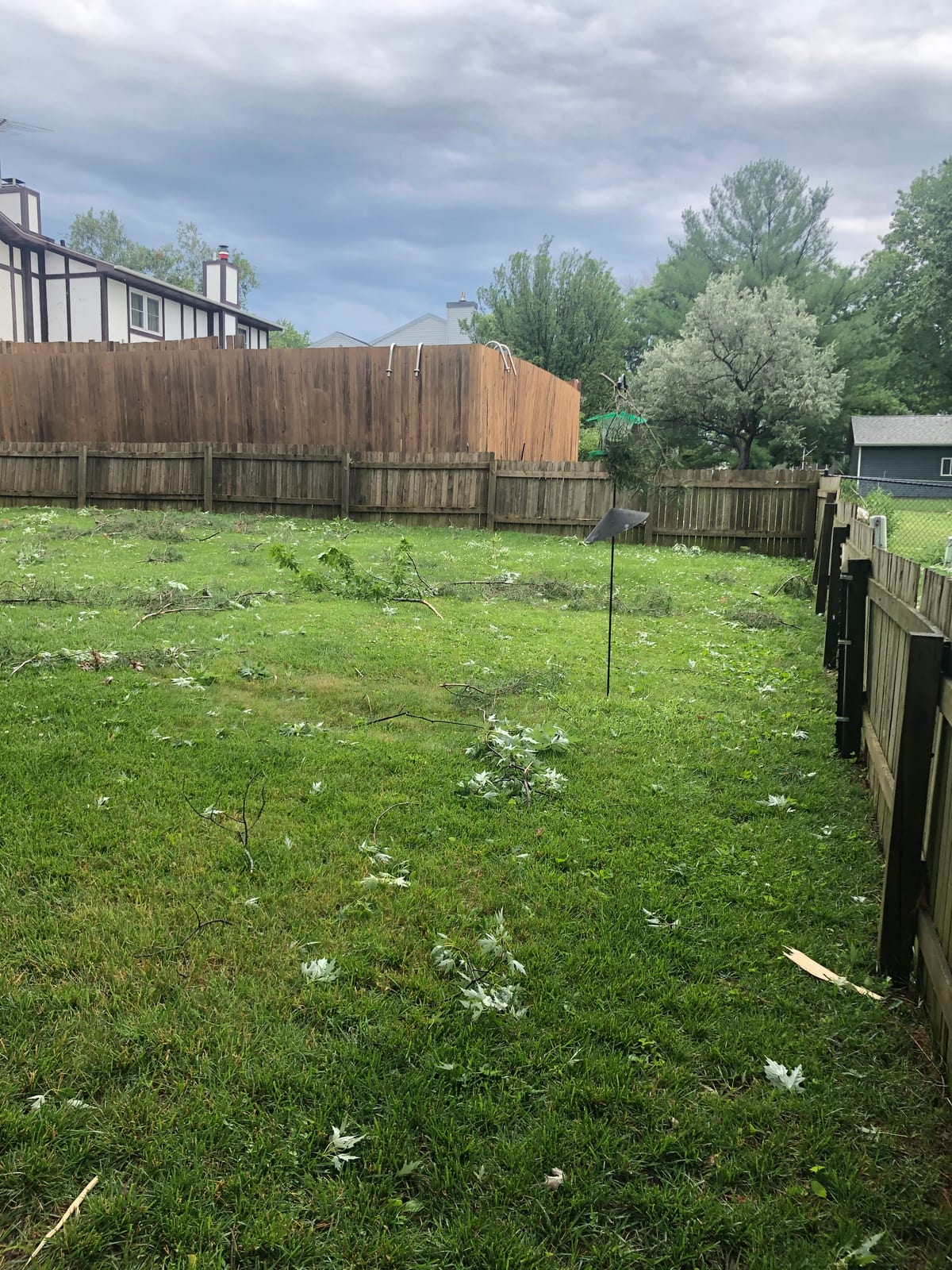 Deck and lawn littered with downed branches under a cloudy sky
